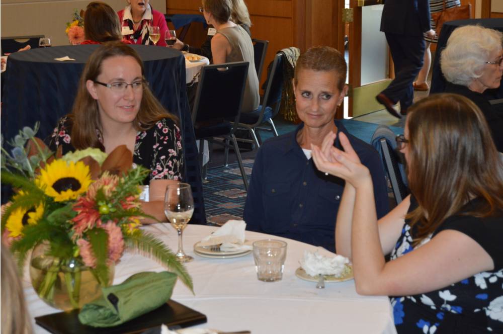 Two alumnae listening to an alumna speak at a table